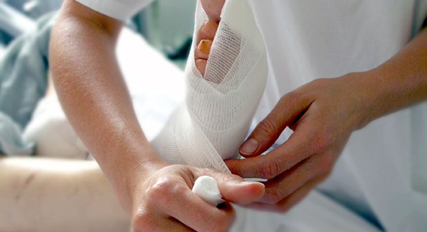 Bild på sjuksköterska som lindar bandage runt en fot