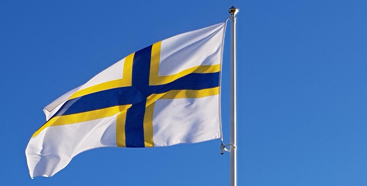 Sverigefinnanrnas flagga mot blå himmel.
